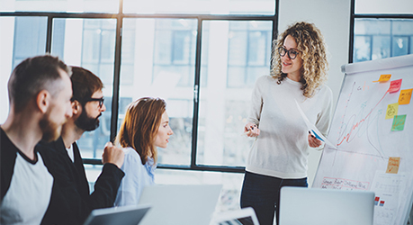 Weibliche Führungskraft, die zwei Männern und einer Frau etwas an einem Flipchart erklärt.