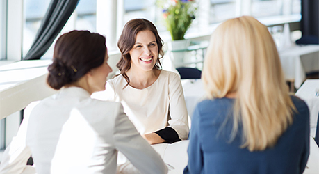 Weibliche Führungskraft im freundlichen Gespräch mit zwei Mitarbeiterinnen, die mit dem Rücken zum Betrachter sitzen