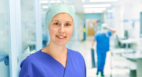 Auf dem Bild sieht man eine junge Frau in OP-Kleidung in einer leicht verschwommenen Krankenhausumgebung.